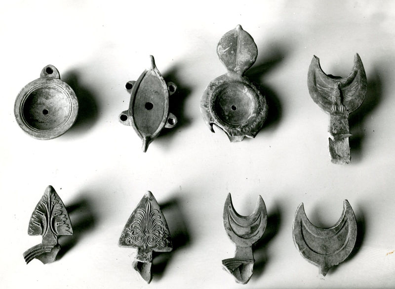 002703 - reperto - Casa Repubblicana a fianco delle Scalae Caci (sud-ovest della Casa di Livia), ambiente I, colmatura (scarico superficiale di terra arenosa), durante gli scavi del Carettoni del 1956.  Lucerne di varie tipologie : (da sinistra in alto) lucerna monolicne, lucerna tetraliene a forma di barca, lucerna ad ansa bilobata e anse di varie forme (triangolare decorata, semilunare ecc).

Bibliografia: Carettoni, G.F. in NsC 1967 pag.307

Neg. serie F nÂ°2397